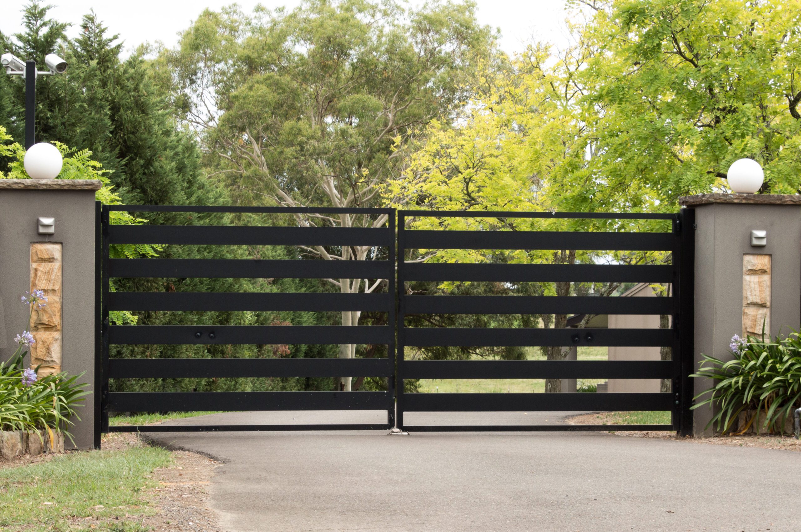Black metal driveway entrance gates set in brick fence Rénovation et menuiserie à Levignac
